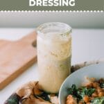 Caesar dressing in jar on the table with a kitchen towel and bowl of salad