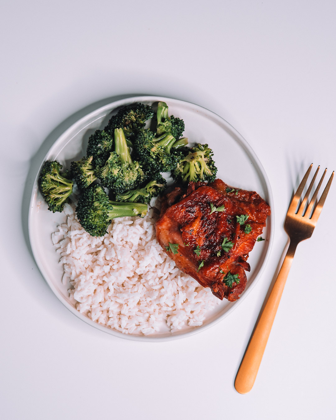 Instant Pot Honey Garlic Chicken on white round plate with a bed of white rice and freshly roasted green broccoli with gold fork.