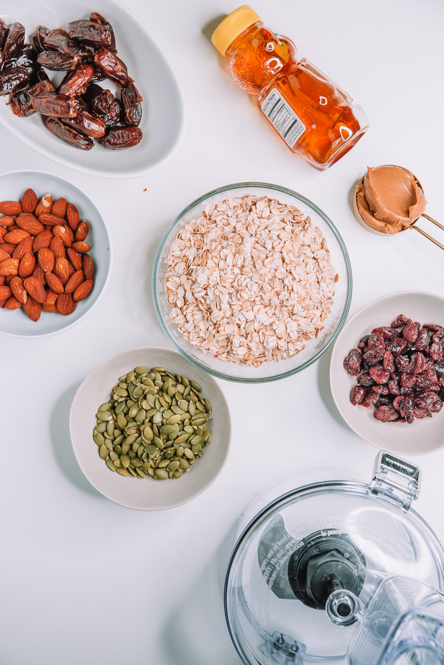 Old fashioned oats, pitted dates, honey, dried cranberries, pumpkin seeds on a white table.