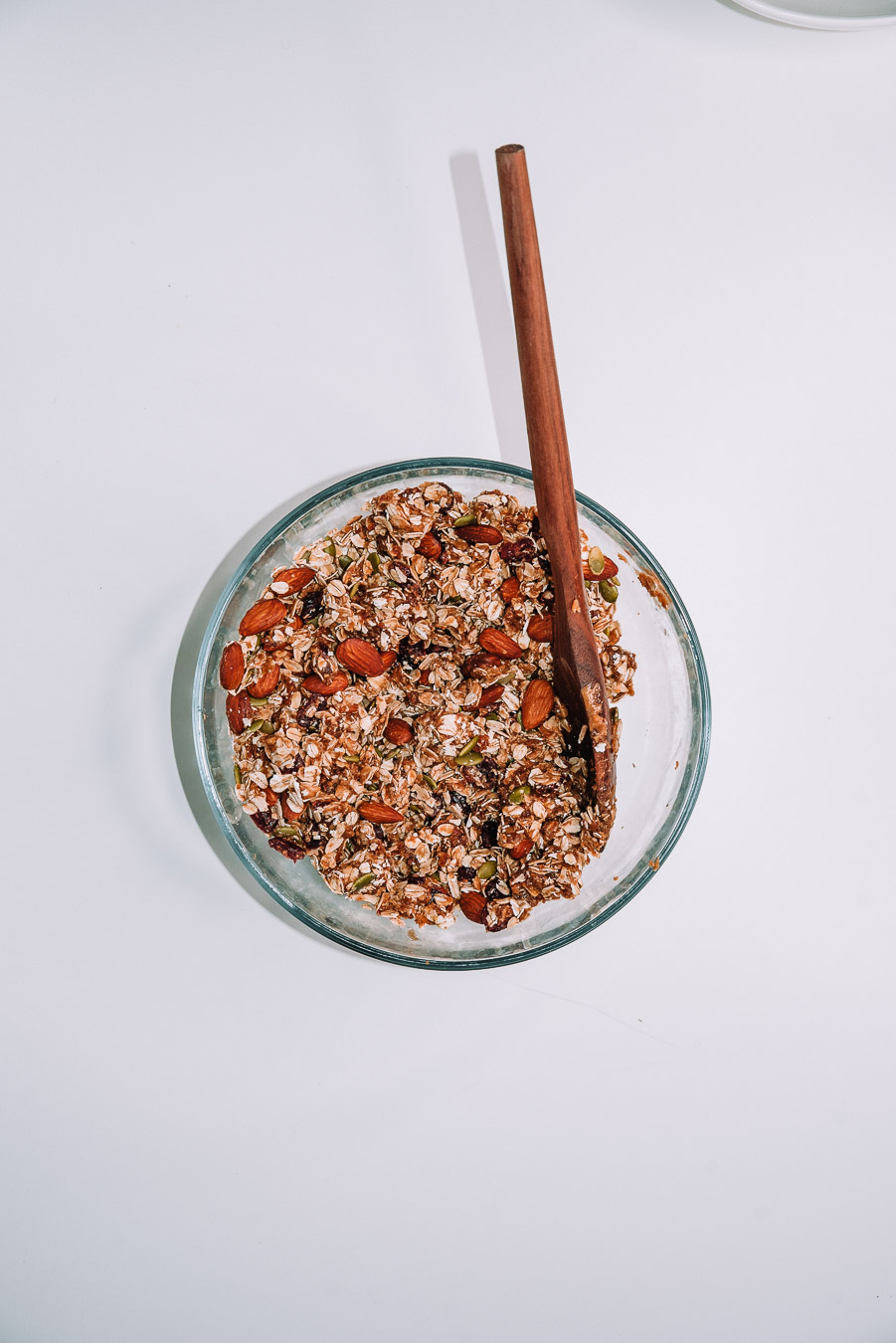 Freshly made granola mixed together in clear bowl placed on white table 