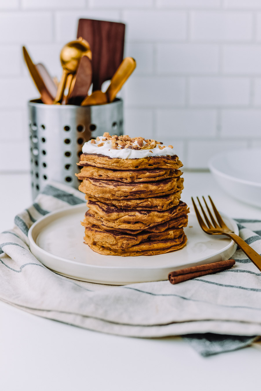 Stack of oatmeal pancakes on a white plate sitting on top of a kitchen towel on a white table. 