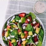 Bowl filled with strawberries, spinach, avocado, on a grey and white kitchen towel