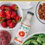 Bowl filled with strawberries, spinach, avocado, on a grey and white kitchen towel