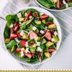 Bowl filled with strawberries, spinach, avocado, on a grey and white kitchen towel