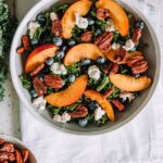 Bowl filled with kale, peaches, goat cheese, blueberries