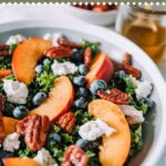 Bowl filled with kale, peaches, goat cheese, blueberries