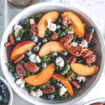 Bowl filled with kale, peaches, goat cheese, blueberries