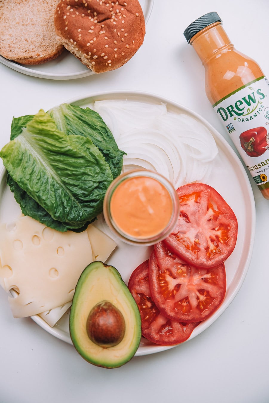 Tomatoes, onion, lettuce, cheese slices, avocado, and thousand island dressing on a plate with a bottle