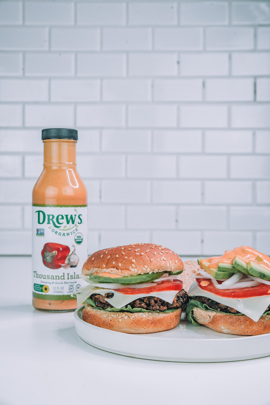 2 black bean burgers on a white plate with a bottle of thousand island dressing