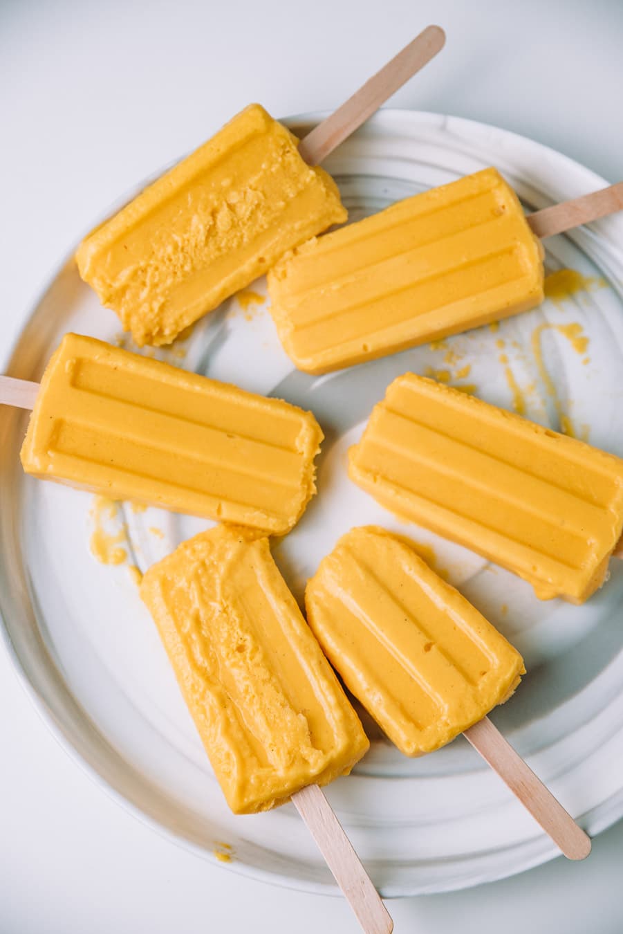 Melting mango lassi popsicles on a plate