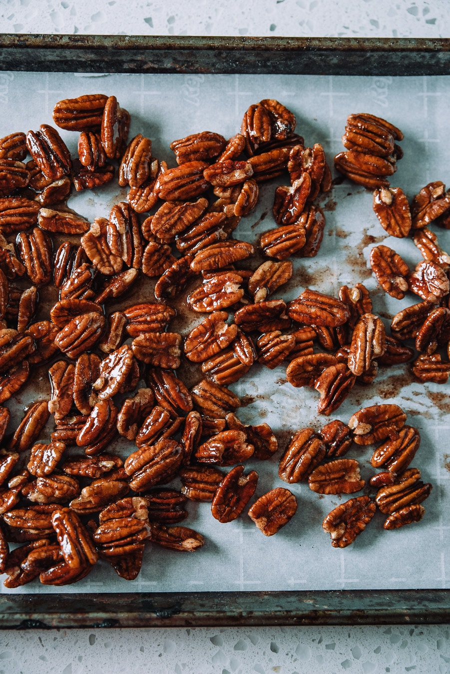 Candied pecans on a parchment lined baking sheet.