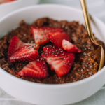 Thick of bowl of chocolate oatmeal with strawberries and chia seeds.