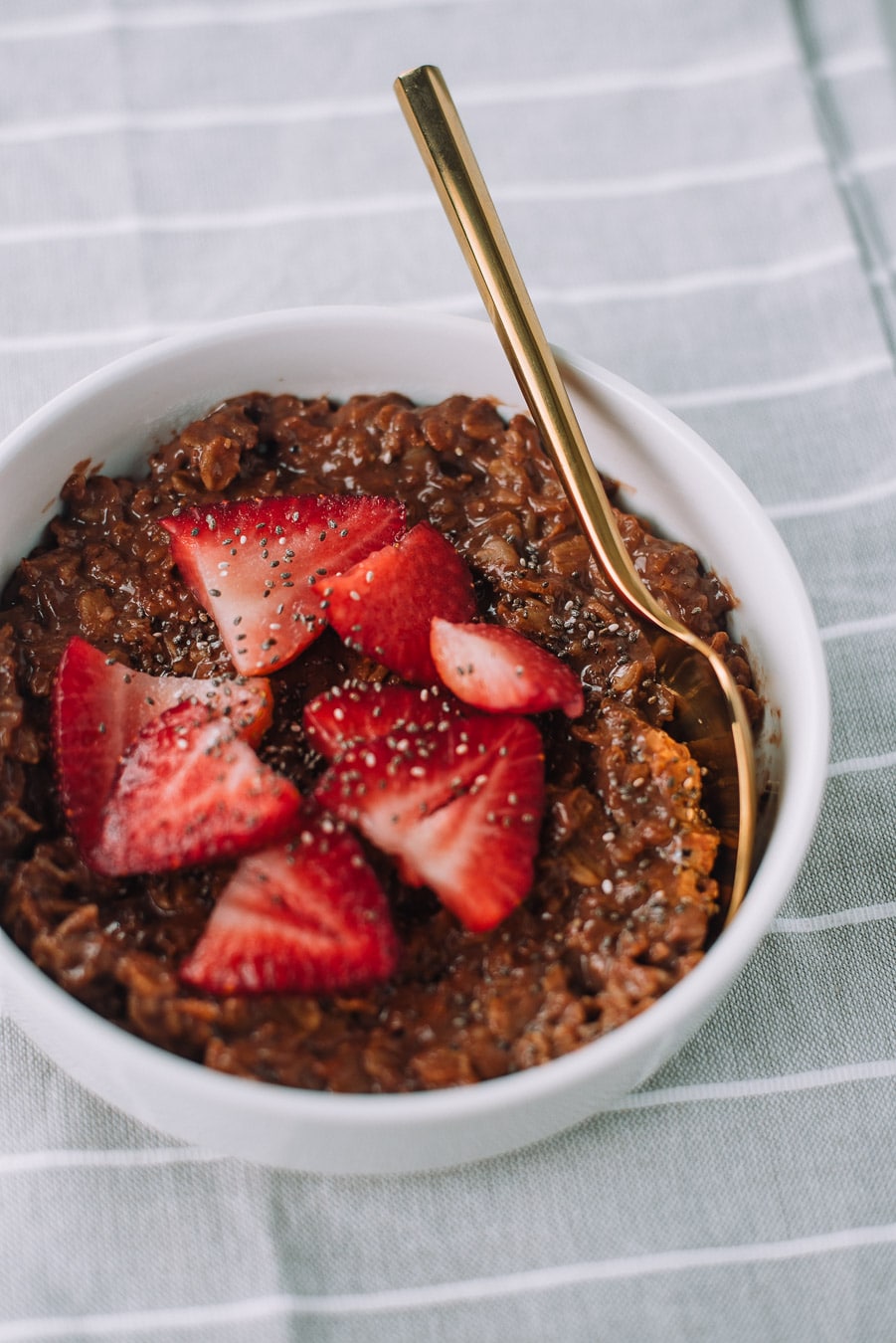 Thick of bowl of chocolate oatmeal with strawberries and chia seeds. 