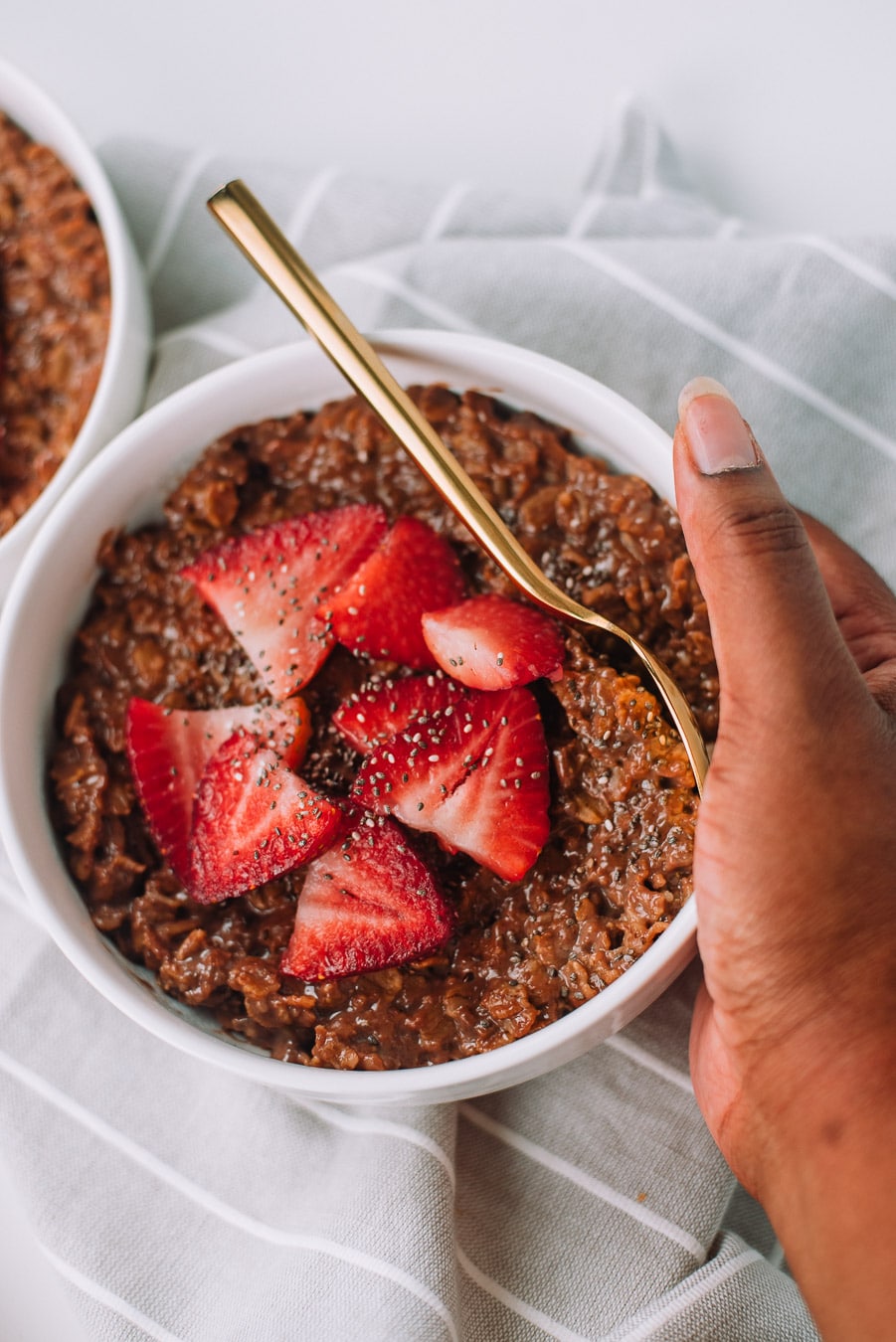 Hand holding a thick of bowl of chocolate oatmeal with strawberries and chia seeds. 