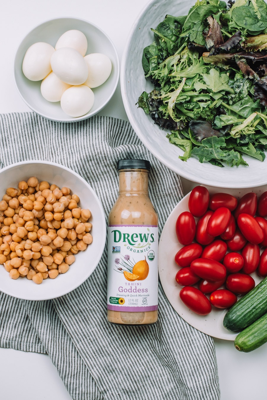 Bowls of mixed greens, boiled egg, grape tomatoes, mini cucumbers, chickpeas, and Drew's Organics Tahini Goddess Dressing and Marinade