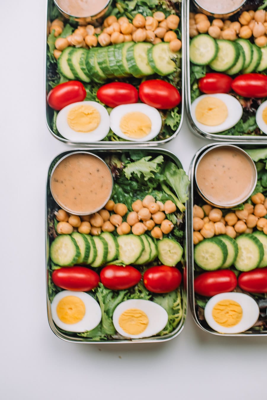 4 Bento boxes filled with mixed greens, boiled egg, grape tomatoes, mini cucumbers, chickpeas, and Drew's Organics Tahini Goddess Dressing and Marinade