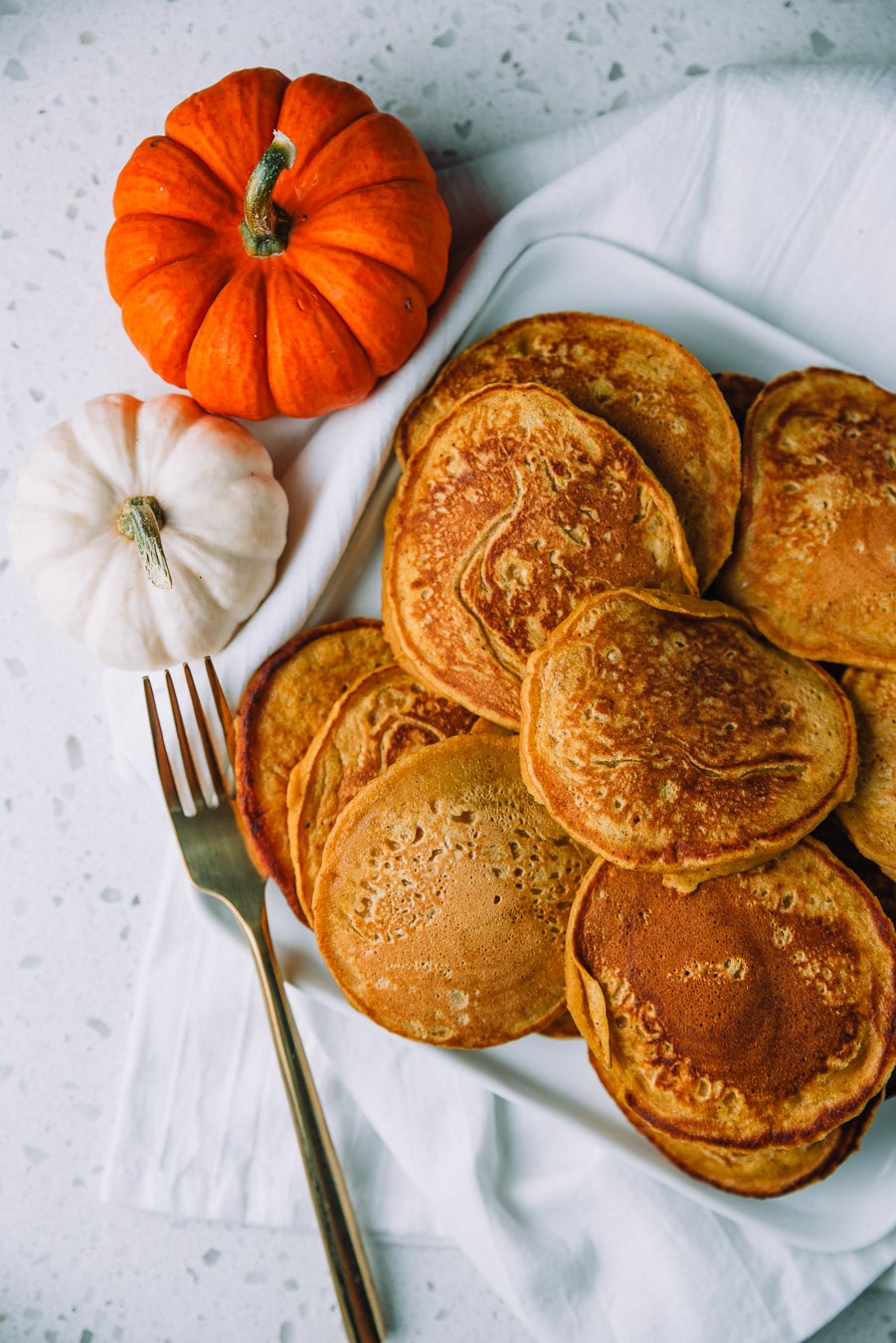 Easy Pumpkin Pancakes piled on a square plate placed on a white napkin on a countertop