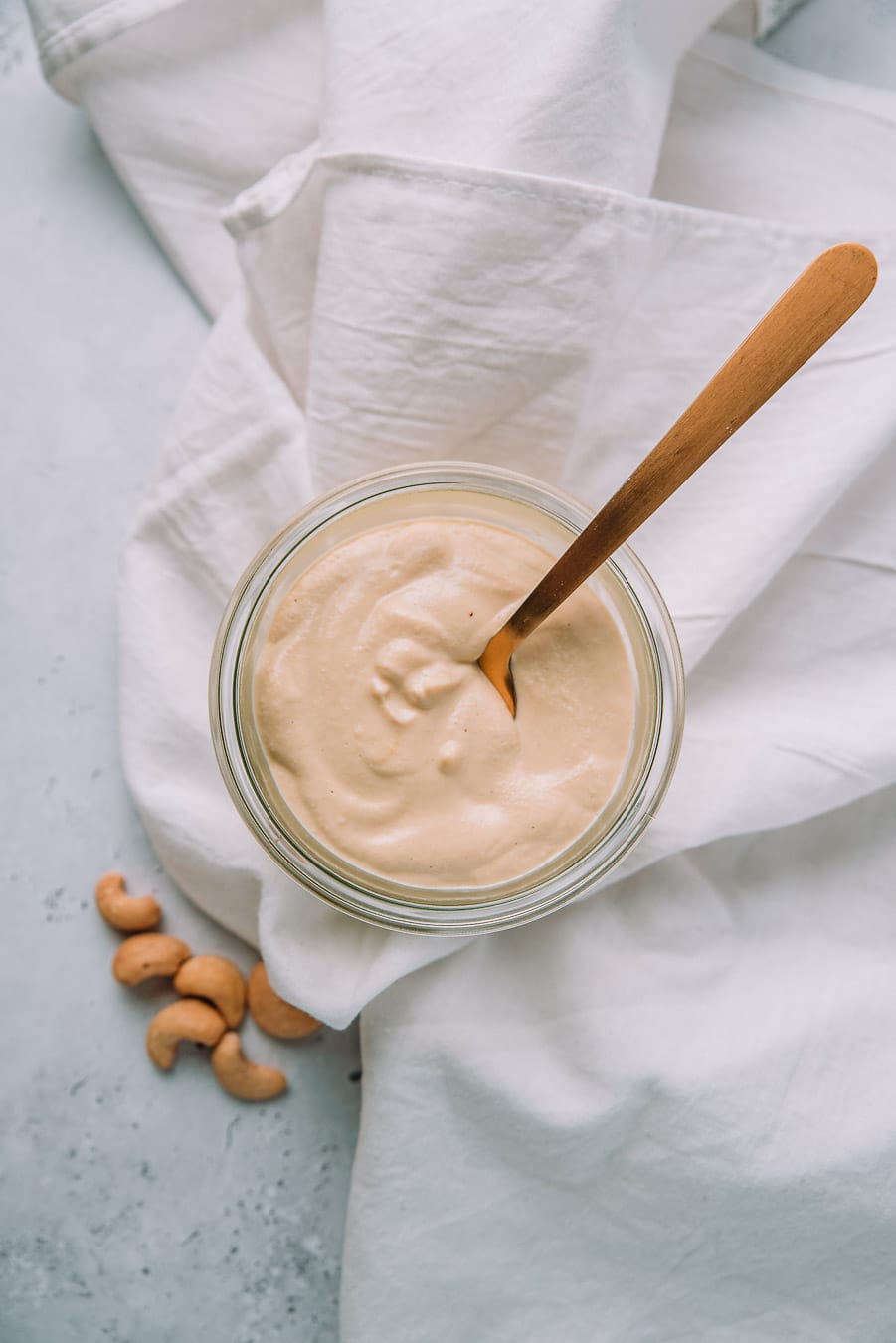 Cashew Alfredo Sauce in a jar with a gold spoon next to a jar of cashews, lemon, and a bulb of garlic