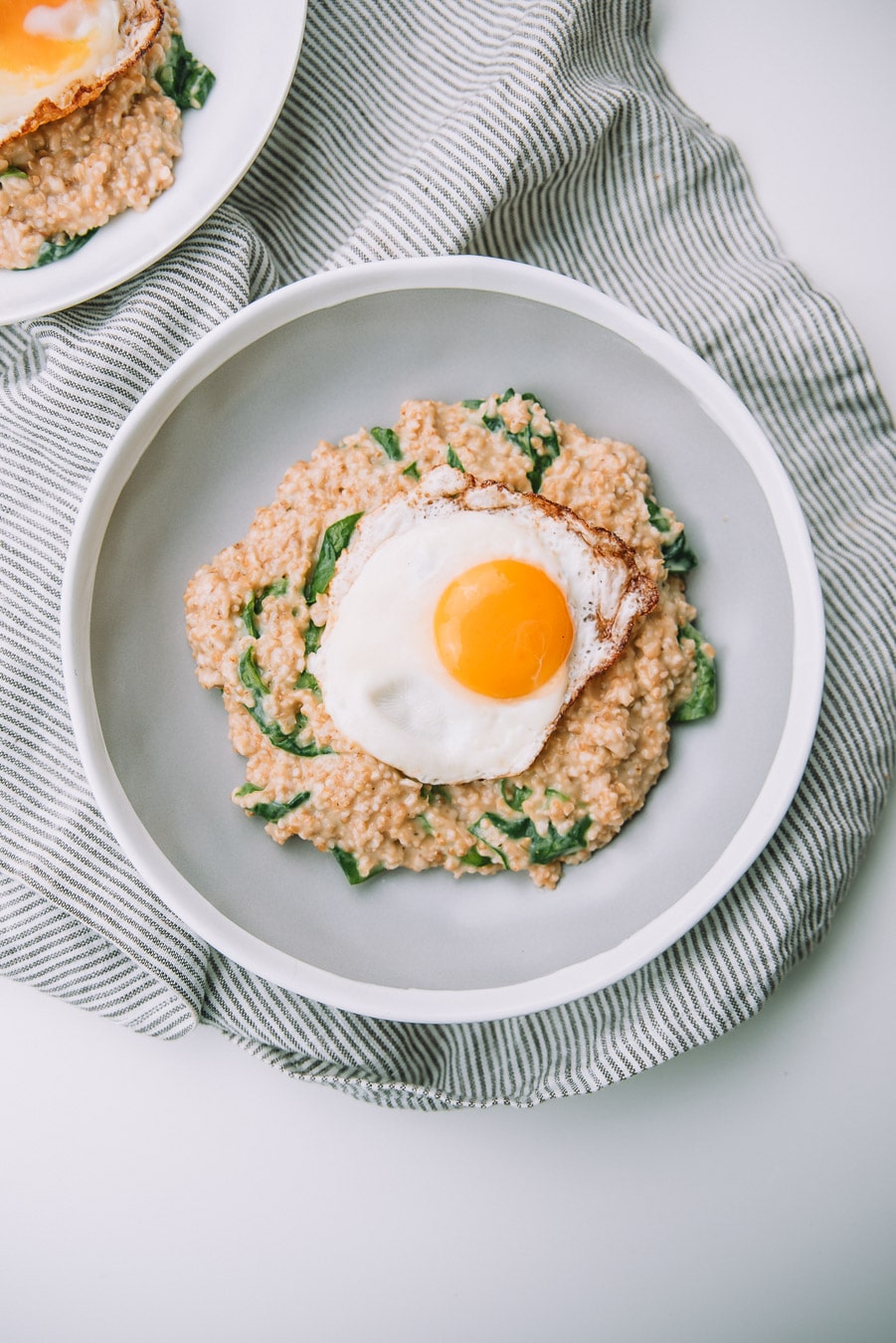 Bowl of Savory Spinach Oatmeal with Fried Eggs with a kitchen towel