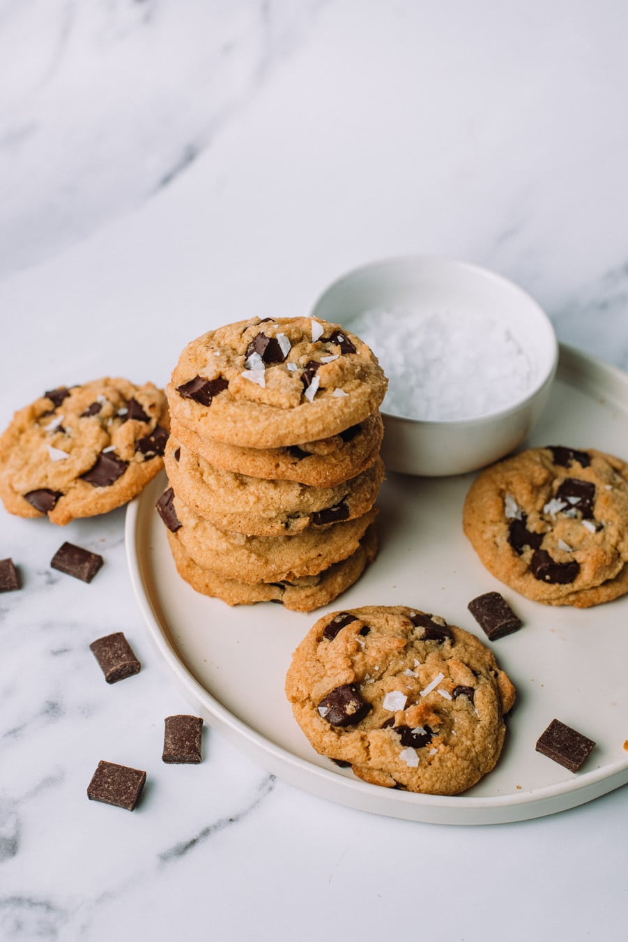 Olive Oil Chocolate Chip Cookies stacked on top of each other on a white plate with extra chocolate morsels.