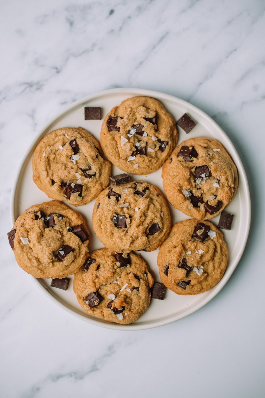 Olive Oil Chocolate Chip Cookies stacked on top of each other on a white plate with extra chocolate morsels.