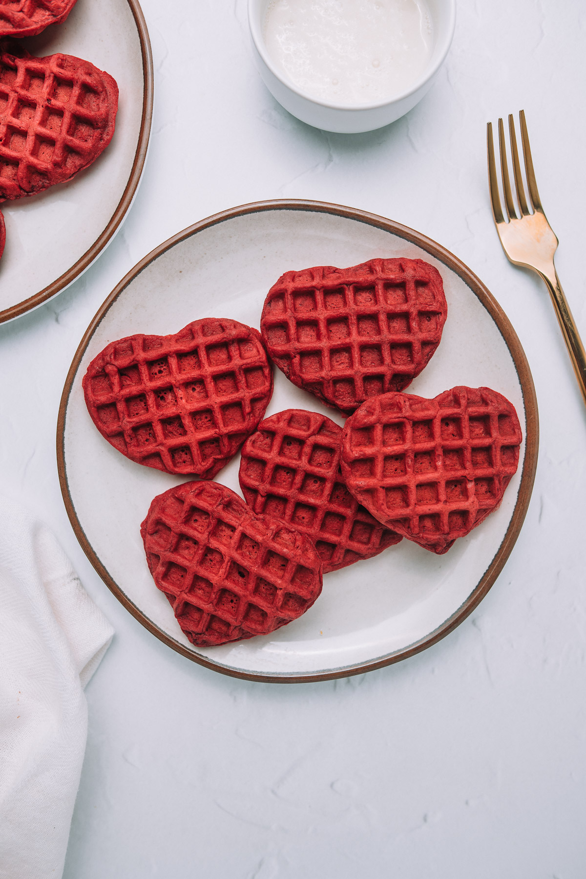 Buttermilk Red Velvet Waffles on a plate sitting on a white table with a gold fork. 