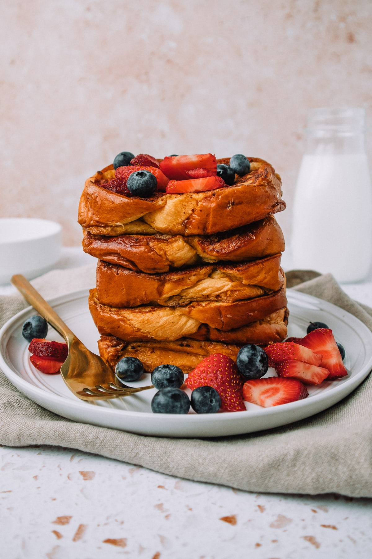 Delicious slices of brioche french toast stacked on a plate with fresh strawberries and blueberries for a yummy breakfast or brunch