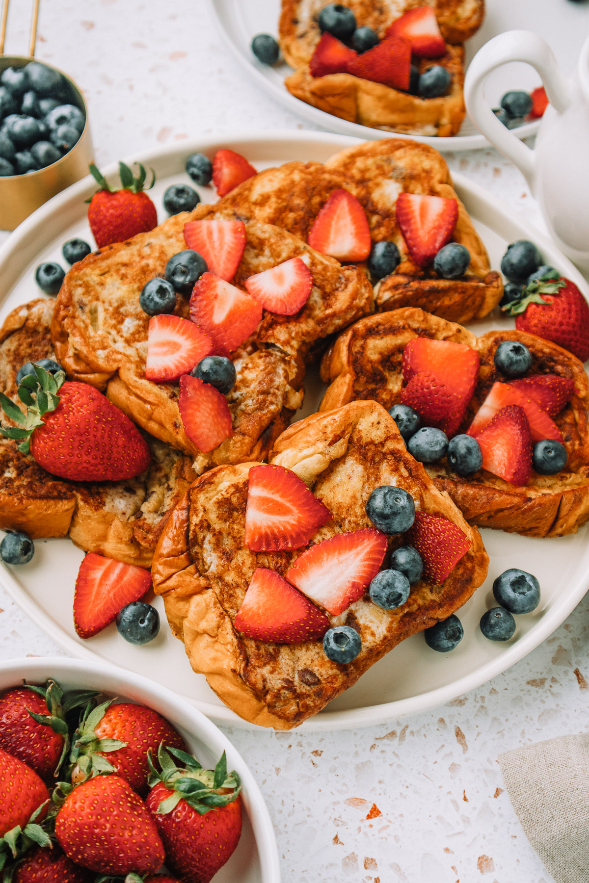 Delicious slices of brioche french toast stacked on a plate with fresh strawberries and blueberries for a yummy breakfast or brunch