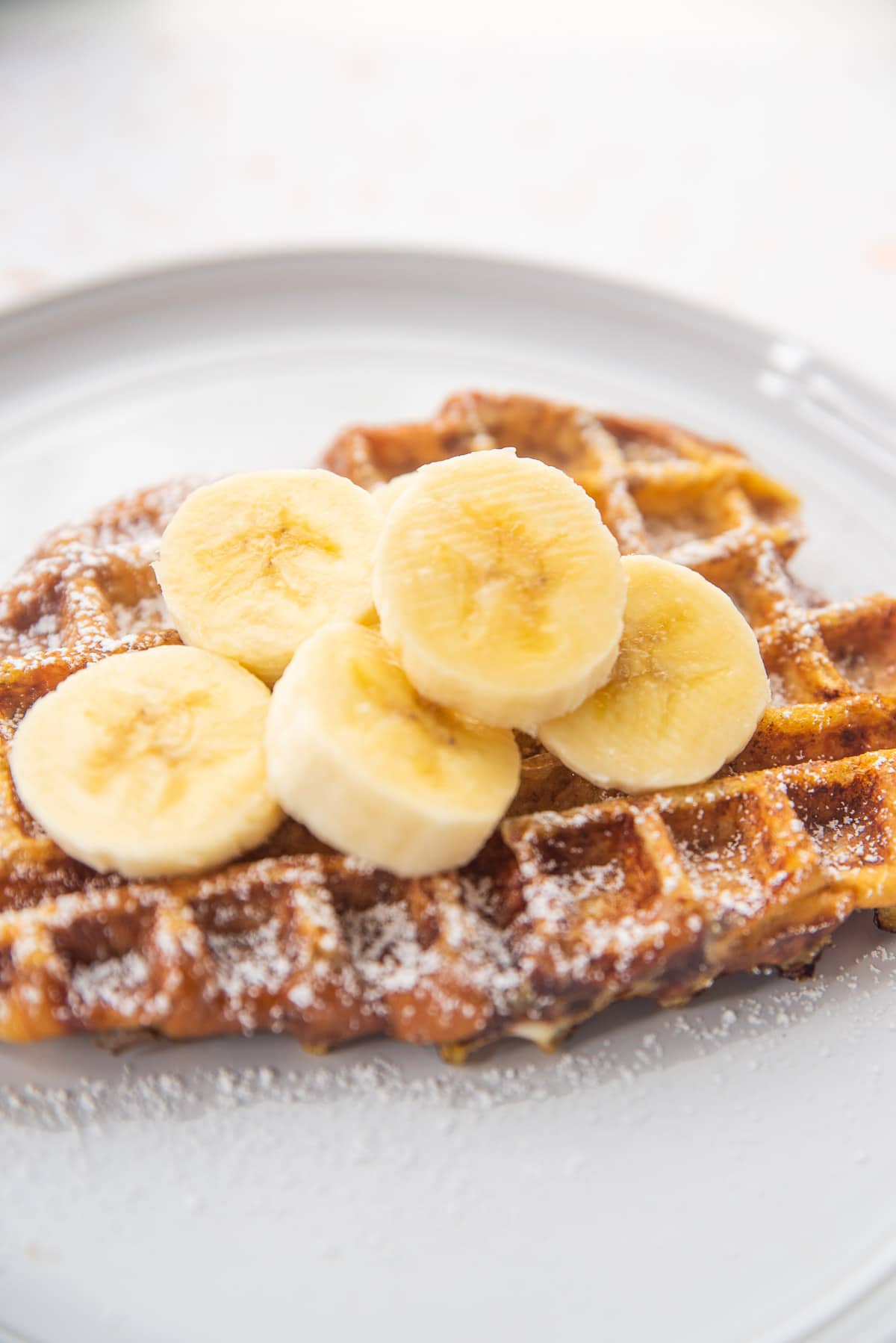 French toast waffles topped with powdered sugar and sliced bananas. 