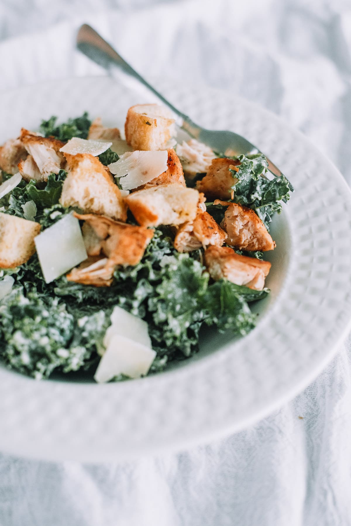 Kale Caesar Salad with Chicken with croutons in a white bowl with silver fork